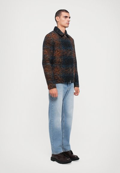Woolen jacket with a blue, orange, and black pattern, featuring a collar and a front zipper. Paired with light wash denim and black shoes.