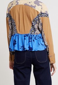 Vícebarevná košile s květinovými a puntíkovanými vzory. Má nabraný modrý spodní lem, dlouhé rukávy a kombinaci texturovaných látek.