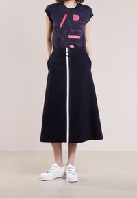 Námořnická sukně s pruhy, se zipem vpředu a kulatým kovovým detailem, kombinovaná s černým grafickým tričkem a bílými teniskami.