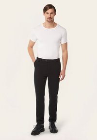 Witte, korte mouwen t-shirt gecombineerd met zwarte broek. De broek heeft een gladde textuur en een enkele voorkantzak. Zwarte schoenen met veters.