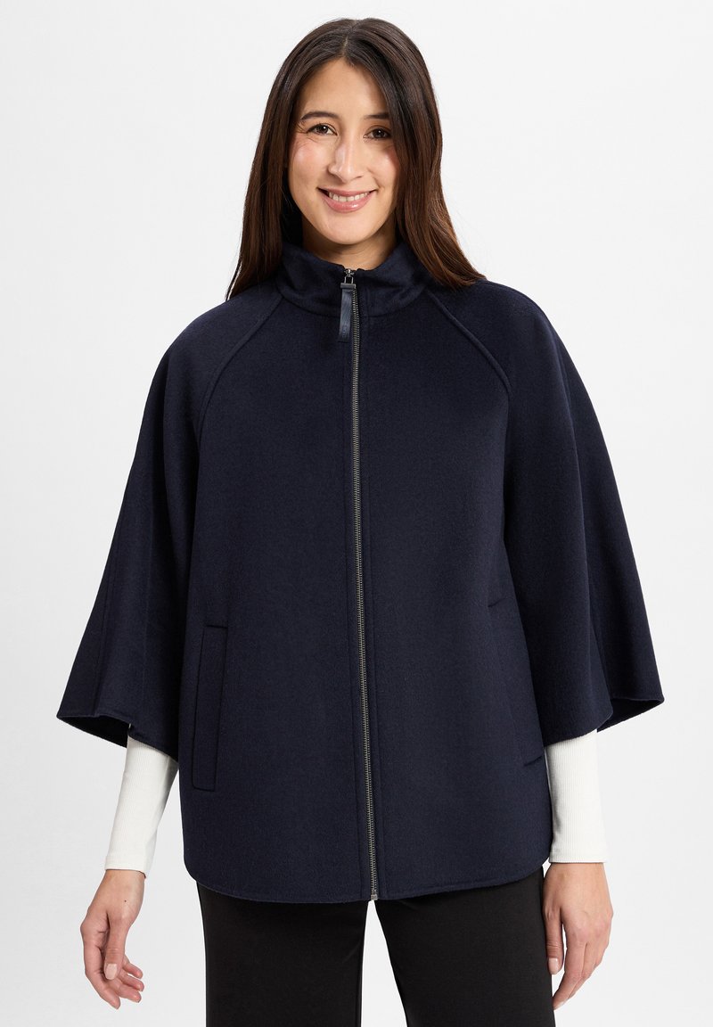 Cape en mélange de laine bleu marine avec fermeture éclair, col haut et poches latérales. Présente un design ample et fluide ainsi qu'une texture douce.