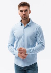 Camisa de botones de manga larga en azul claro con cuello y textura acanalada. Combinada con jeans de mezclilla informales.