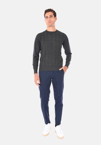 Maglione in morbido punto treccia verde scuro abbinato a chinos blu navy e sneakers bianche. Il maglione ha un collo rotondo e polsini e orlo a costine.