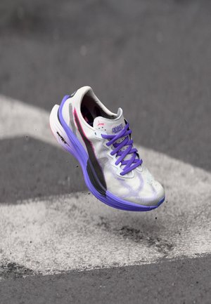 Weiße Sportschuh mit strukturiertem Obermaterial, lila Akzenten und einem schwarzen Seitenstreifen. Leichtes Design mit gepolsterter Sohle, ideal für Leistung.