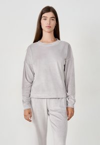 Felpa in velluto grigio chiaro con maniche lunghe, scollo tondo e vestibilità comoda. Tessuto morbido, design minimalista, abbinata a pantaloni coordinati.