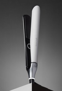 Witte en zwarte ghd Chronos stijltang staand op een grijze ondergrond met een gradiënt grijze achtergrond.