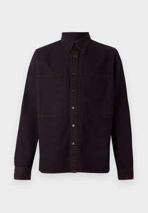 Camisa de mezclilla de color púrpura oscuro con mangas largas, un cuello puntiagudo, dos bolsillos frontales y costuras rojas en contraste. Cuenta con cierre de botones.
