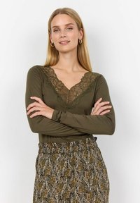 Olijfgroen lang mouw top met een kanten V-hals. Gecombineerd met een gemusterde rok in aardetonen, met een paisley ontwerp.