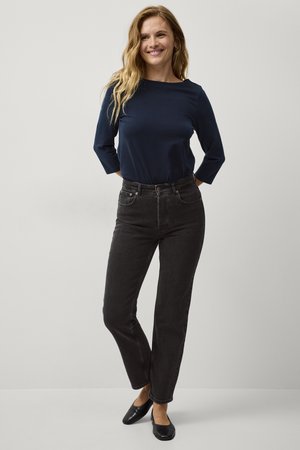 Navy blauwe lange mouwen top gecombineerd met hoge taille zwarte jeans, met voorzakken en een rechte broekspijp, aangevuld met zwarte flats.