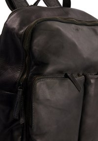 Czarny skórzany plecak o gładkiej fakturze, z wyraźnym zamkiem błyskawicznym i dwoma przednimi kieszeniami. Subtelne akcenty w postaci szwów podkreślają design.