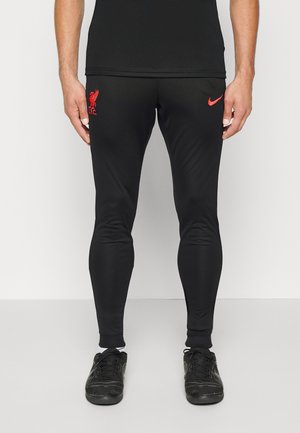 Pantalon de sport noir en tissu lisse et extensible. Présente un logo rouge de Liverpool sur la cuisse gauche et des poignets de cheville côtelés.