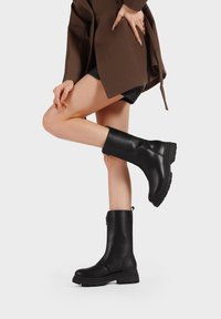 Stivaletti neri alla caviglia in pelle liscia, con zip laterale, suola spessa e punta arrotondata. Design leggermente texturizzato con un pratico passante.