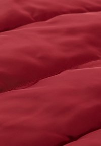 Raudona, paminkštinta medžiaga su lygiu tekstūra, turinti susiūtą siūlę ir šiek tiek blizgų paviršių, pabrėžianti švelnumą ir šilumą.