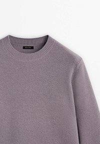 Pull en maille mauve clair avec un col rond, des poignets côtelés et une surface texturée. Étiquette visible au niveau du cou.