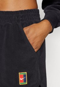 Mustad musta fliisist lühikesed püksid, millel on elastne vöökoht ja küljetasku. Märkimisväärne Nike logo söötma kirju ruudukujulises disainis vasakul all. 