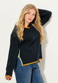 Marine gebreide trui met oranje en groene accenten, voorzien van een bootnek, lange mouwen en een licht asymmetrische zoom.