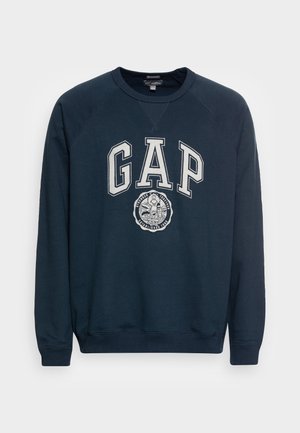 Marinblå sweatshirt med rund halsringning, raglanärmar och stor "GAP"-logotyp i vitt med en cirkulär grafik nedanför. Bomullsblandning.