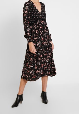 Abito floreale nero con maniche lunghe, scollatura a V, vita arricciata, gonna a strati, caratterizzato da motivi floreali rosa e bianchi, abbinato a stivaletti neri.