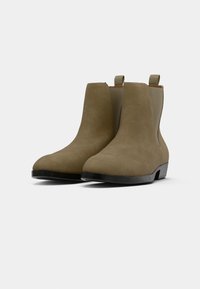 Olivově zelené semišové kotníkové boty s zaoblenou špičkou, elastickými bočními panely a poutky na stažení. Černé gumové podešve pro lepší trakci a trvanlivost.