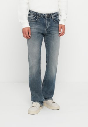 Vaqueros de denim azul claro con corte recto, zonas desgastadas y diseño tradicional de cinco bolsillos. Combinados con zapatillas blancas.