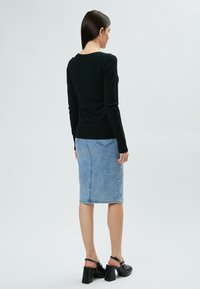 Pull noir en maille avec un col rond et des poignets côtelés, associé à une jupe crayon en denim bleu clair avec des détails de coutures au dos. Chaussures à talons noires.