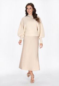 Crème gebreid pull met pofmouwen, versierde halslijn; gecombineerd met een beige satijnen maxi rok en metallic hakken met straps.