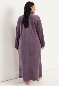 Lång, lila plyschrock med långa ärmar, rak skärning och en mjuk textur. Har en söm längs ryggen och når anklarna.