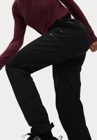 Zwarte outdoorbroek met een gladde textuur, voorzien van een ritszak en een relaxte pasvorm, gecombineerd met een bordeauxrode longsleeve top.