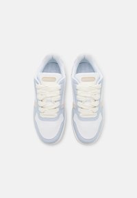 Bílé a světle modré tenisky s texturovanými materiály, kulatou špičkou, polstrovaným límcem, krémovými tkaničkami a malou лог döžkou na jazyku.