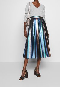 Metallic pleated skirt features blue, green, and bronze stripes; paired with a gray sweater and black heeled sandals. Bag in hand.