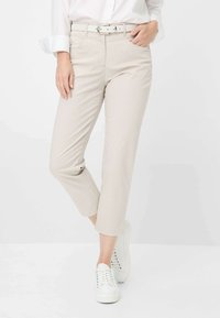 Hellbeige, hochgeschnittene Hosen mit einem strukturierten Muster, ausgestattet mit einem passenden Gürtel und Seitentaschen, kombiniert mit weißen Sneakers.