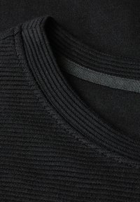 Dettaglio in tessuto a coste nero con un colletto texture e uno strato liscio sottostante. Il tessuto ha una finitura opaca e cuciture sottili.