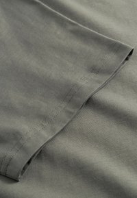 Țesătură de bumbac gri cu textură netedă, prevăzută cu un tiv curat și detalii subtile de cusătură de-a lungul marginii. Vedere de aproape a materialului.