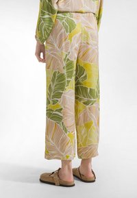 Pantalones de pierna ancha con una base de color amarillo brillante y un gran patrón de hojas en verde y durazno, hechos de tela ligera.