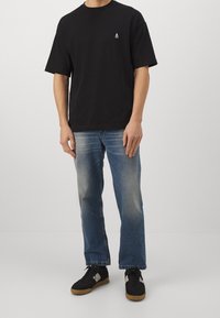 Sort t-shirt med korte ærmer og et lille logo på brystet, parret med slidte blå straight-leg jeans og sorte sneakers med gummisåler.