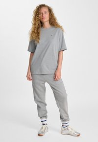  camiseta de algodón gris, ajuste holgado, mangas cortas, combinada con pantalones de chándal grises. Acentos a rayas blancas, azules y marinas en los calcetines; zapatillas plateadas.