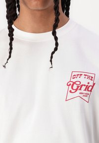 White cotton t-shirt featuring a red graphic design with the text "OFF THE GRID" in a bold font on the left chest area.