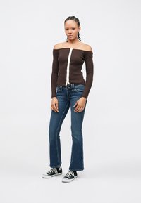 Haut marron côtelé à épaules dénudées avec une patte de boutonnage centrale, associé à un jean bleu évasé et des baskets noires avec des accents blancs.