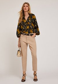 Satinblus i flera färger med ballongärmar; beige skräddarsydda byxor; svart bälte; guldfärgad handväska; svarta sandaler med remmar.