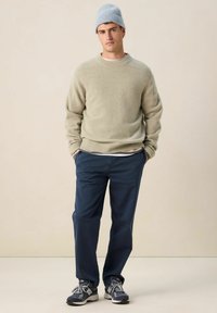 Pull en maille vert clair, pantalon bleu marine et baskets grises. Un bonnet en maille bleu complète le look. Design simple, textures douces.