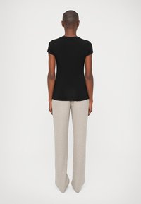Tricou negru, ajustat, cu mâneci scurte, purtat cu pantaloni lejeri, largi, de un bej deschis, evidențiind un material texturat și un design cu picioare drepte.