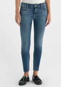 Jean skinny en jean délavé moyen, avec cinq poches, une fermeture à bouton et fermeture éclair, et un design classique et épuré. Associé à des mocassins noirs.