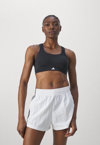 Svart idretts-BH med rund hals, paret med hvite shorts med svarte side-striper. Glatt tekstur, tettsittende design og elastisk midjebånd.