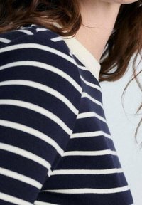 Modrý a bílý pruhovaný pletený top s kulatým výstřihem. Má hladkou texturu a krátké rukávy, které zdůrazňují střídající se barevný vzor.