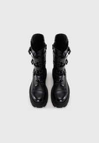 Black leather combat boots with a round toe, front lacing, and three adjustable straps featuring metal buckles. Thick rubber soles.