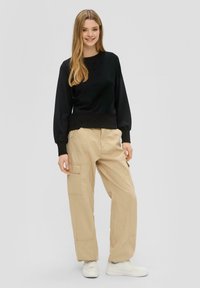 Zwarte lange mouw pullover met een geribde zoom, gecombineerd met beige cargobroek met zijzakken en opgerolde enkels, gedragen met witte sneakers.