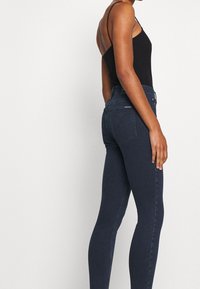 Smala jeans i mörkblå denim med en slät yta och minimal söm. Högmidjad design med vanliga fickor och bälteshällor.