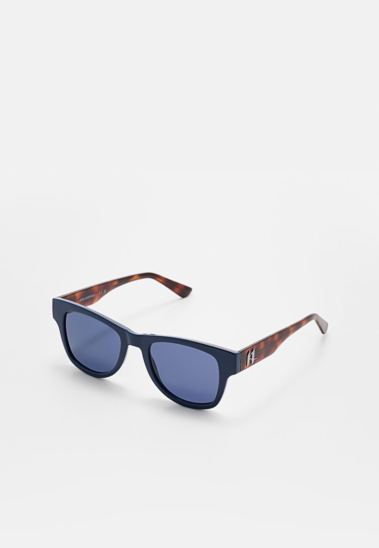 Lunettes de soleil avec une monture épaisse bleu marine, des verres bleu foncé et des branches en écaille de tortue marron avec un détail de logo.