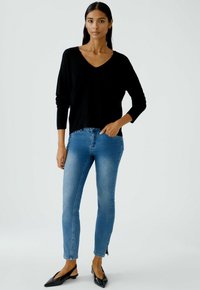 Schwarzer V-Ausschnitt-Pullover mit langen Ärmeln, kombiniert mit hellblauenSlim-Fit-Jeans und schwarzen spitzen Ballerinas. Die Jeans haben eine dezente Ausbleichung.