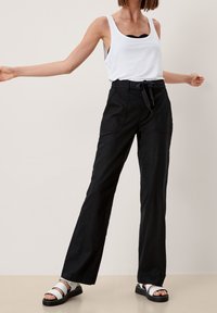 Pantalon noir à jambes larges avec une taille ajustable à nouer, doté de deux poches latérales. Associé à un débardeur blanc et des sandales noires et blanches.